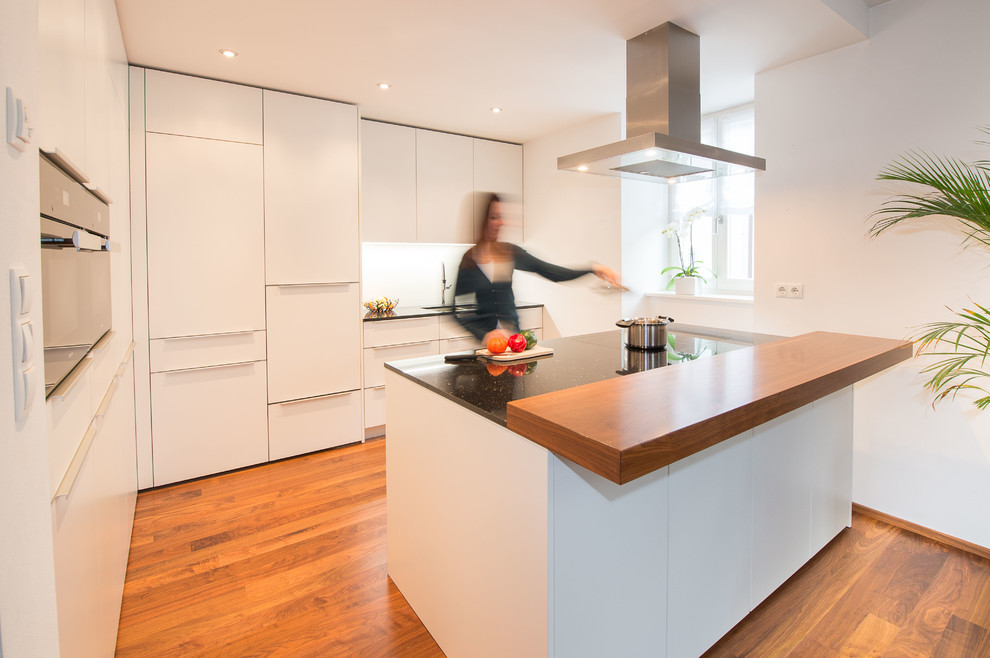 This is an example of a mid-sized contemporary l-shaped eat-in kitchen in Other with an undermount sink, flat-panel cabinets, white cabinets, solid surface benchtops, white splashback, stainless steel appliances, medium hardwood floors and with island.