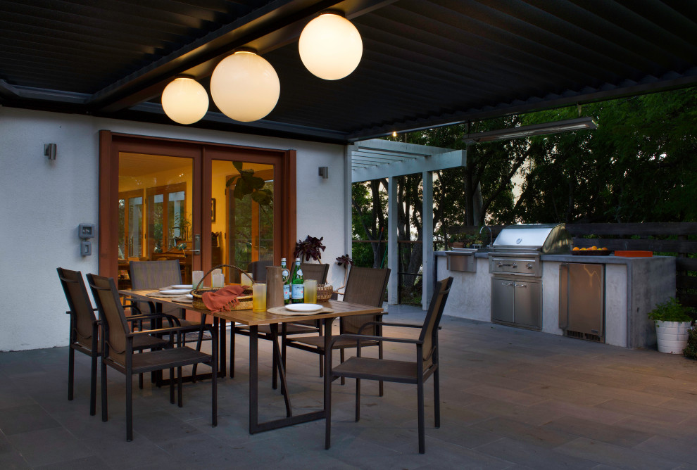 Exemple d'une grande terrasse arrière tendance avec des pavés en pierre naturelle, une cuisine d'été et une pergola.