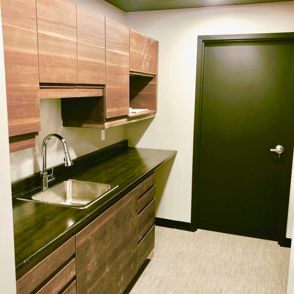 Photo of a small industrial galley separate kitchen with a single-bowl sink, flat-panel cabinets, dark wood cabinets, laminate benchtops, stainless steel appliances, vinyl floors, no island, beige floor and black benchtop.