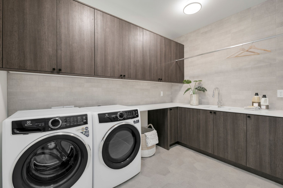 This is an example of a large country l-shaped dedicated laundry room in Seattle with an utility sink, grey cabinets, quartz benchtops, grey splashback, subway tile splashback, grey walls, ceramic floors, a side-by-side washer and dryer, grey floor and white benchtop.