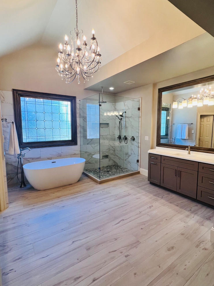 This is an example of a large traditional ensuite bathroom in Atlanta with shaker cabinets, beige cabinets, a freestanding bath, a corner shower, a one-piece toilet, white tiles, beige walls, wood-effect flooring, a submerged sink, engineered stone worktops, grey floors, a hinged door, white worktops, a wall niche, a single sink, a built in vanity unit and a vaulted ceiling.
