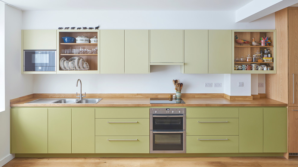 Inspiration for a mid-sized eclectic single-wall open plan kitchen in London with a double-bowl sink, flat-panel cabinets, green cabinets, wood benchtops, panelled appliances, light hardwood floors and no island.