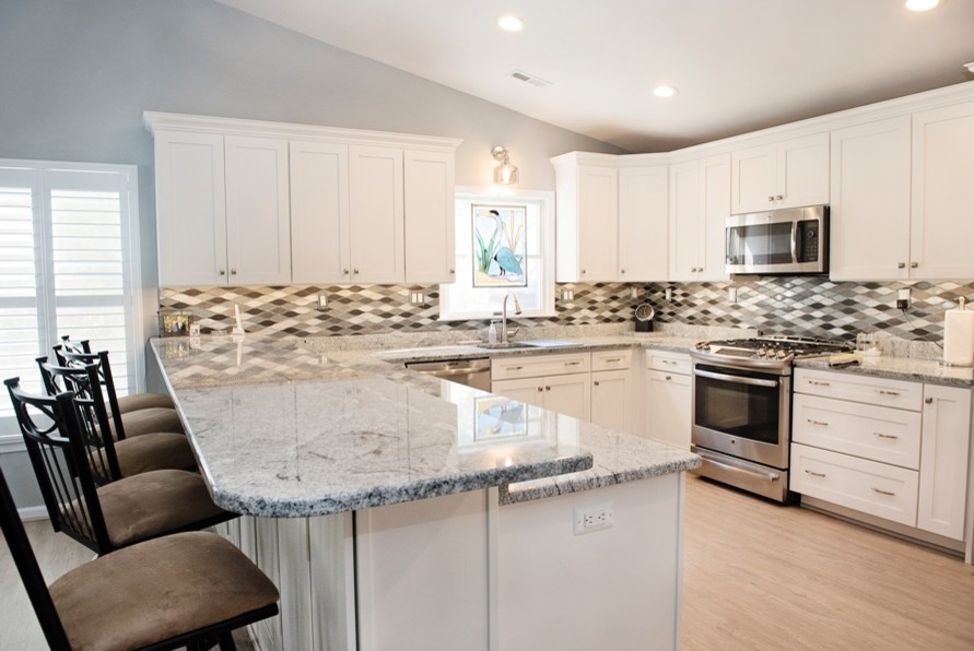 This is an example of a mid-sized contemporary u-shaped open plan kitchen in Baltimore with an undermount sink, shaker cabinets, white cabinets, granite benchtops, glass tile splashback, stainless steel appliances, vinyl floors, with island, grey benchtop, multi-coloured splashback and beige floor.