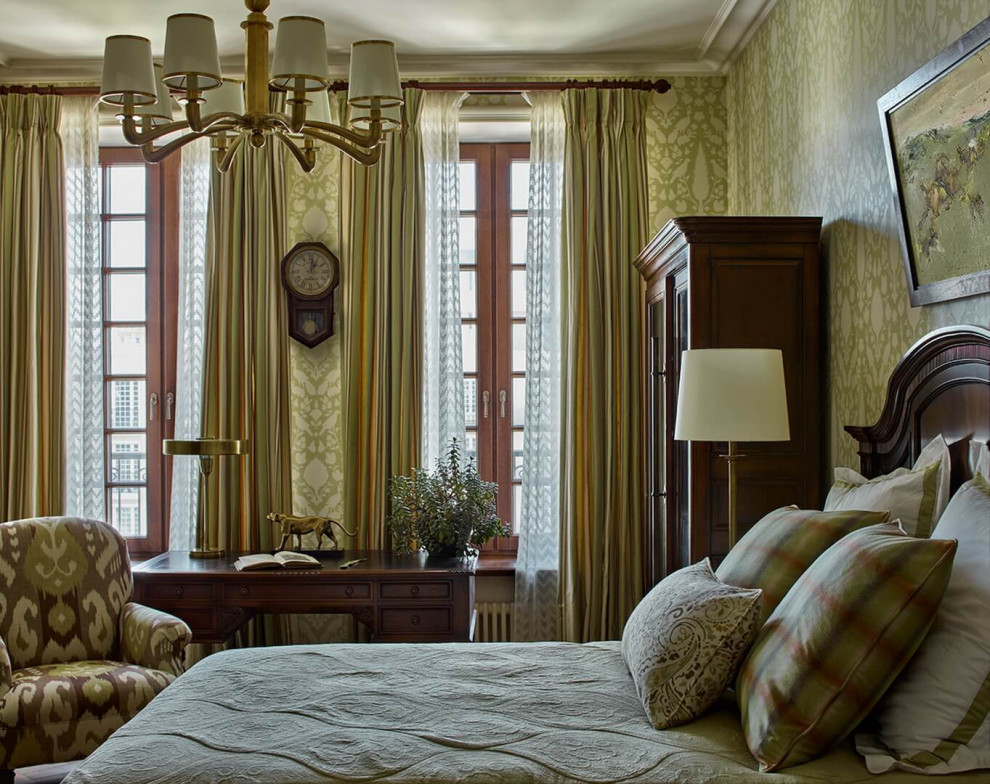 Modelo de dormitorio principal tradicional de tamaño medio sin chimenea con paredes verdes, suelo de madera en tonos medios, suelo marrón y papel pintado