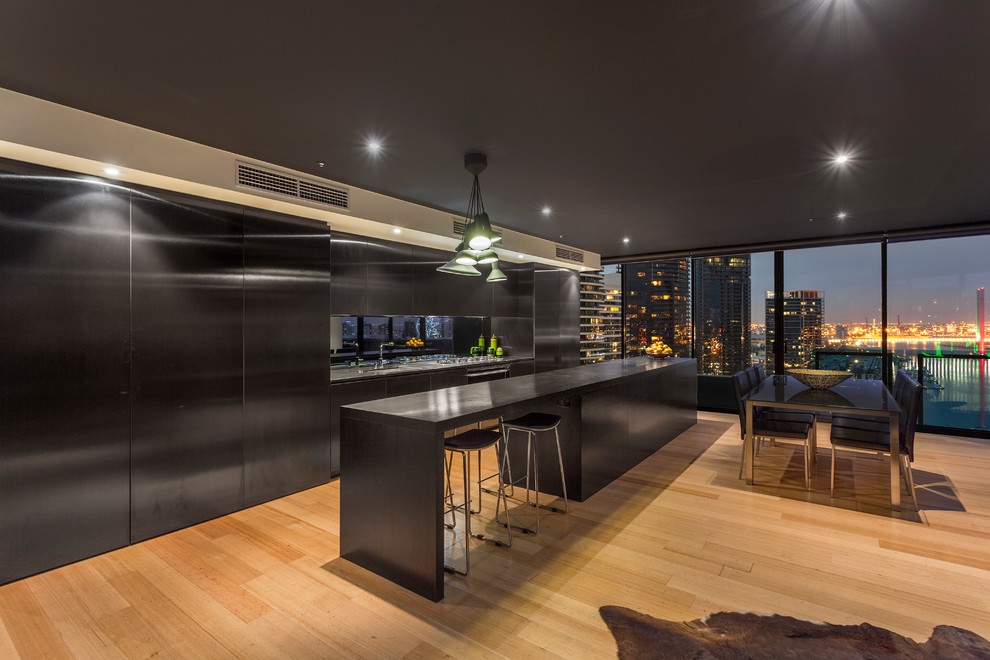 Inspiration for a large contemporary galley eat-in kitchen in Melbourne with a drop-in sink, black cabinets, solid surface benchtops, mirror splashback, black appliances, light hardwood floors and with island.
