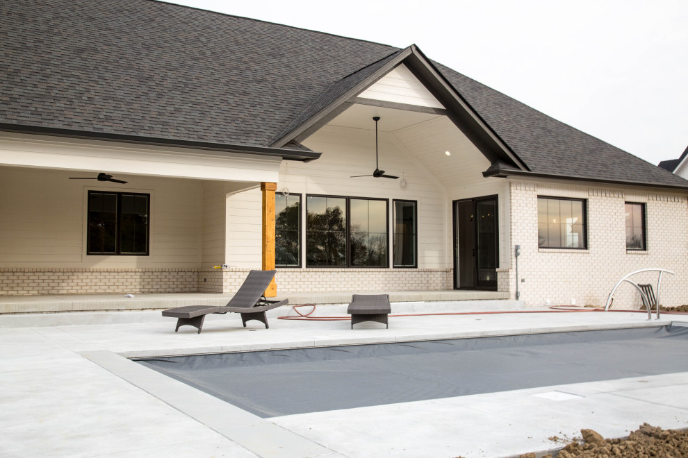 Diseño de piscina natural actual grande rectangular en patio trasero con losas de hormigón