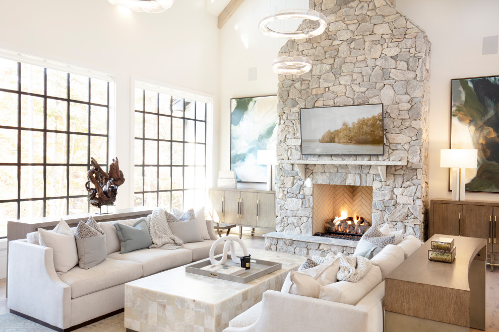 This is an example of a large beach style open concept family room in Other with white walls, light hardwood floors, a standard fireplace, a stone fireplace surround, a wall-mounted tv, brown floor and wood.