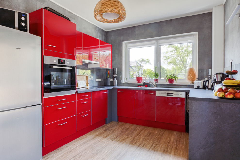 Design ideas for a mid-sized contemporary u-shaped open plan kitchen in Berlin with a drop-in sink, flat-panel cabinets, red cabinets, glass sheet splashback, stainless steel appliances, vinyl floors, no island, brown floor and grey benchtop.