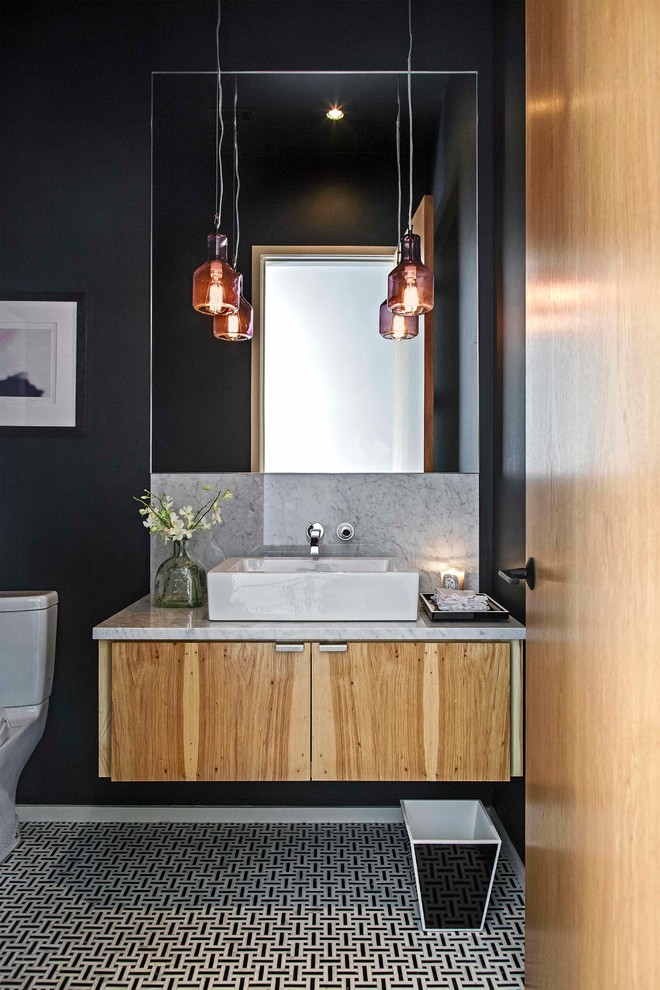 Photo of a small contemporary powder room in Austin with flat-panel cabinets, a vessel sink, marble benchtops, a two-piece toilet, black walls, mosaic tile floors, gray tile, black tile, marble, light wood cabinets and grey benchtops.