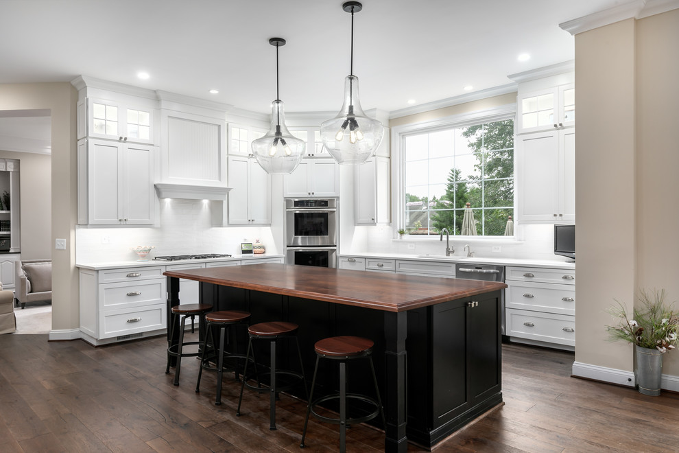 Eat-in kitchen - huge transitional l-shaped dark wood floor and brown floor eat-in kitchen idea in DC Metro with an undermount sink, shaker cabinets, white cabinets, wood countertops, white backsplash, ceramic backsplash, stainless steel appliances, an island and brown countertops