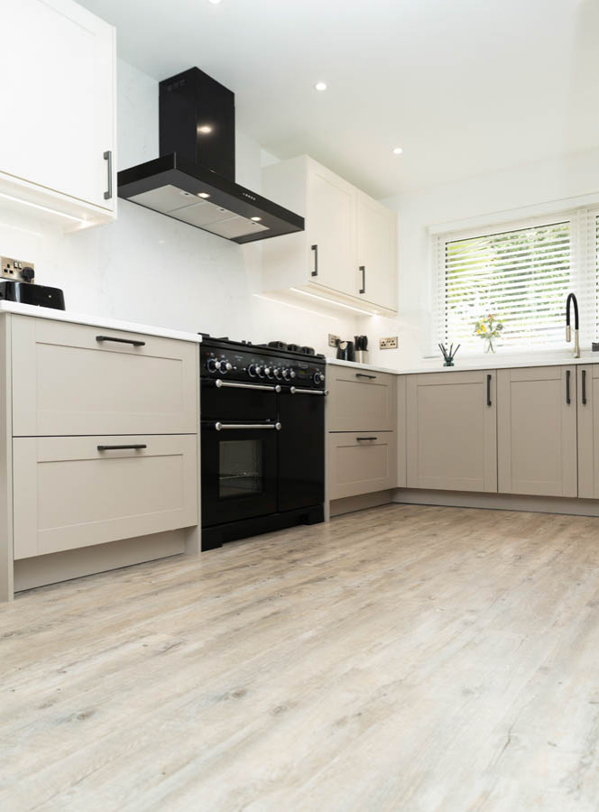 Inspiration for a small contemporary l-shaped open plan kitchen in Manchester with a single-bowl sink, shaker cabinets, white cabinets, quartz worktops, white splashback, black appliances, light hardwood flooring, beige floors and white worktops.