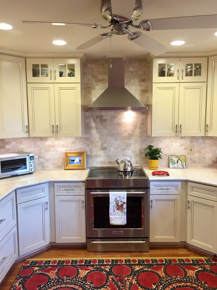 Photo of a transitional kitchen in Boston with recessed-panel cabinets, beige cabinets, marble benchtops, beige splashback, stone tile splashback, stainless steel appliances and light hardwood floors.