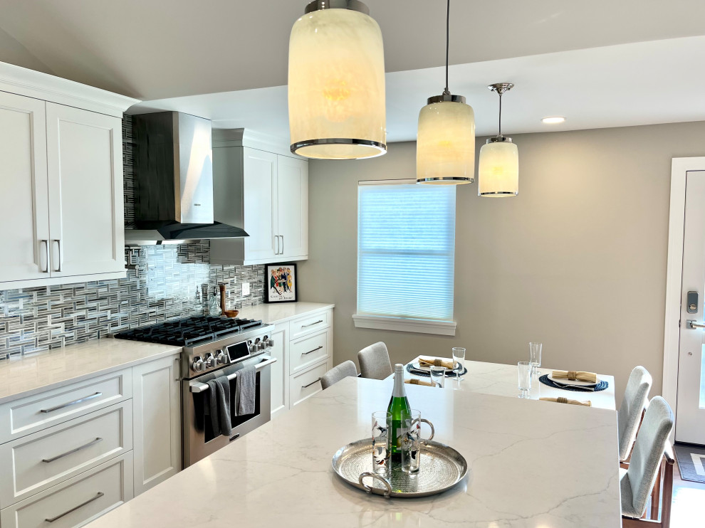 Example of a transitional single-wall vinyl floor, brown floor and vaulted ceiling eat-in kitchen design with an undermount sink, shaker cabinets, white cabinets, quartz countertops, blue backsplash, glass sheet backsplash, stainless steel appliances, an island and gray countertops