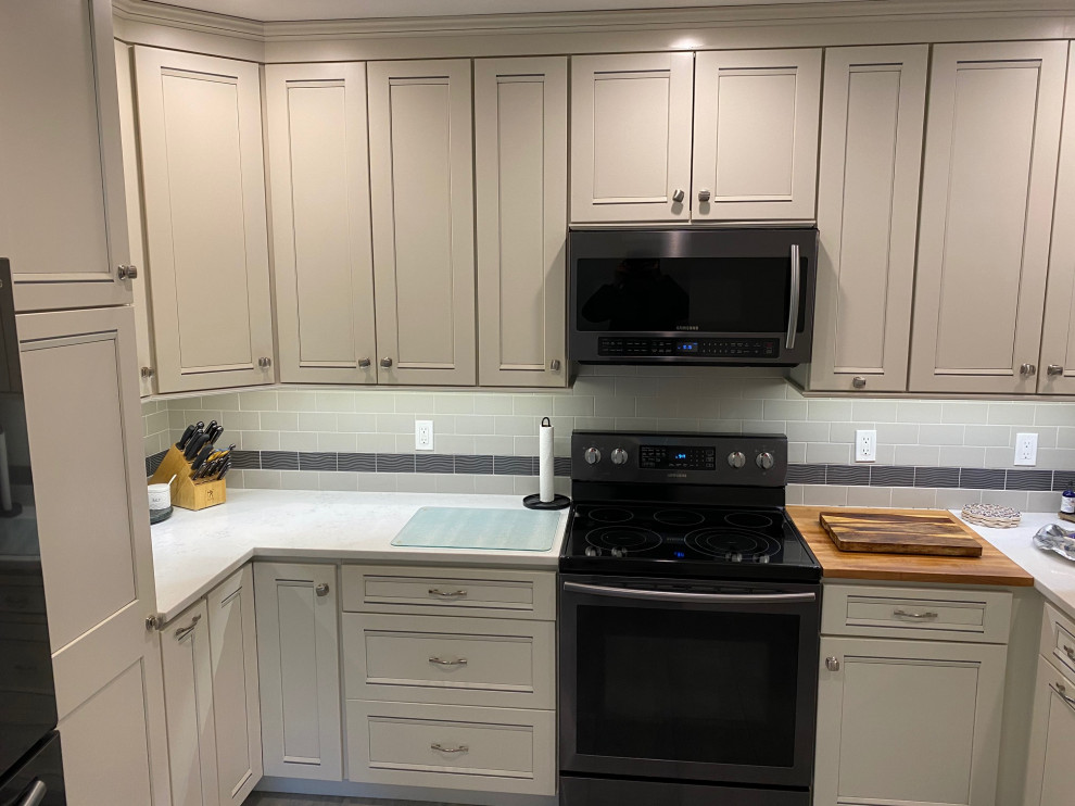Inspiration for a mid-sized transitional u-shaped porcelain tile and gray floor eat-in kitchen remodel in Burlington with a farmhouse sink, recessed-panel cabinets, white cabinets, quartz countertops, gray backsplash, subway tile backsplash, stainless steel appliances and white countertops