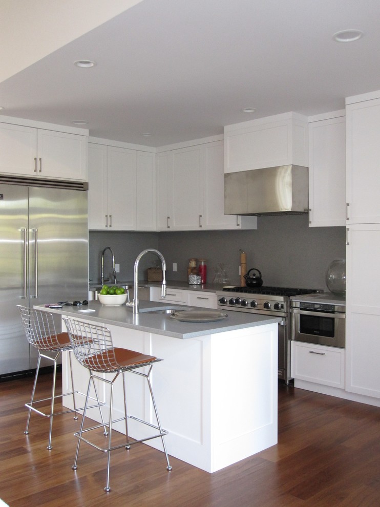 Beach style l-shaped kitchen in New York with an undermount sink, shaker cabinets, white cabinets, grey splashback, stainless steel appliances and grey benchtop.