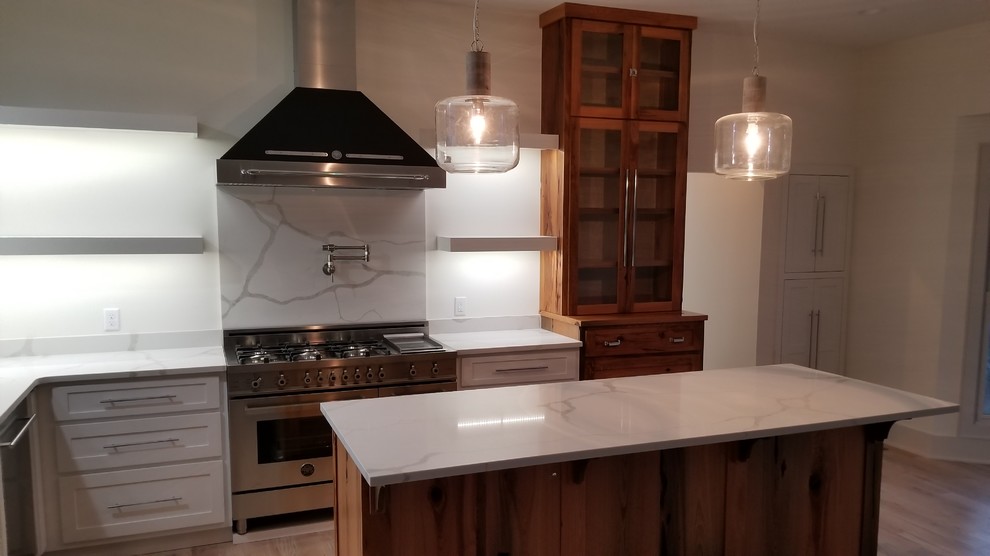 Example of a mid-sized transitional l-shaped light wood floor and brown floor kitchen design with an undermount sink, recessed-panel cabinets, white cabinets, marble countertops, white backsplash, marble backsplash, stainless steel appliances, an island and white countertops