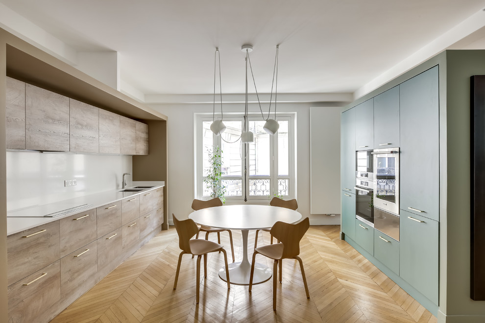 Design ideas for a contemporary galley separate kitchen in Paris with an undermount sink, flat-panel cabinets, green cabinets, white splashback, black appliances, light hardwood floors, no island, beige floor and white benchtop.