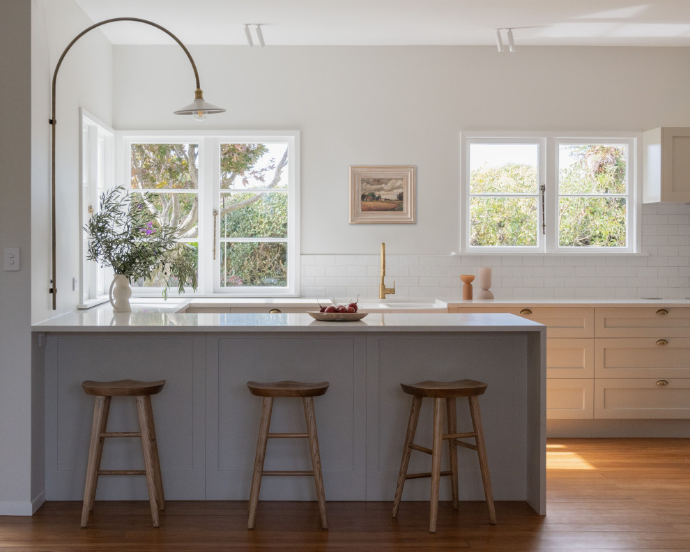 Design ideas for a classic u-shaped kitchen in Hamilton with a belfast sink, shaker cabinets, grey cabinets, white splashback, medium hardwood flooring, a breakfast bar, brown floors and white worktops.