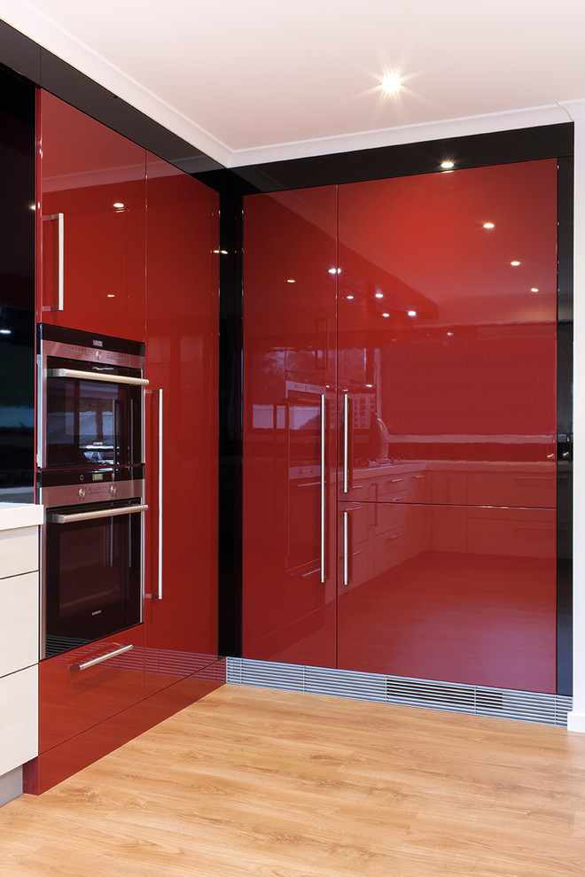 Photo of a large contemporary u-shaped eat-in kitchen in Other with an undermount sink, red cabinets, quartz benchtops, black splashback, glass sheet splashback, stainless steel appliances, light hardwood floors and a peninsula.