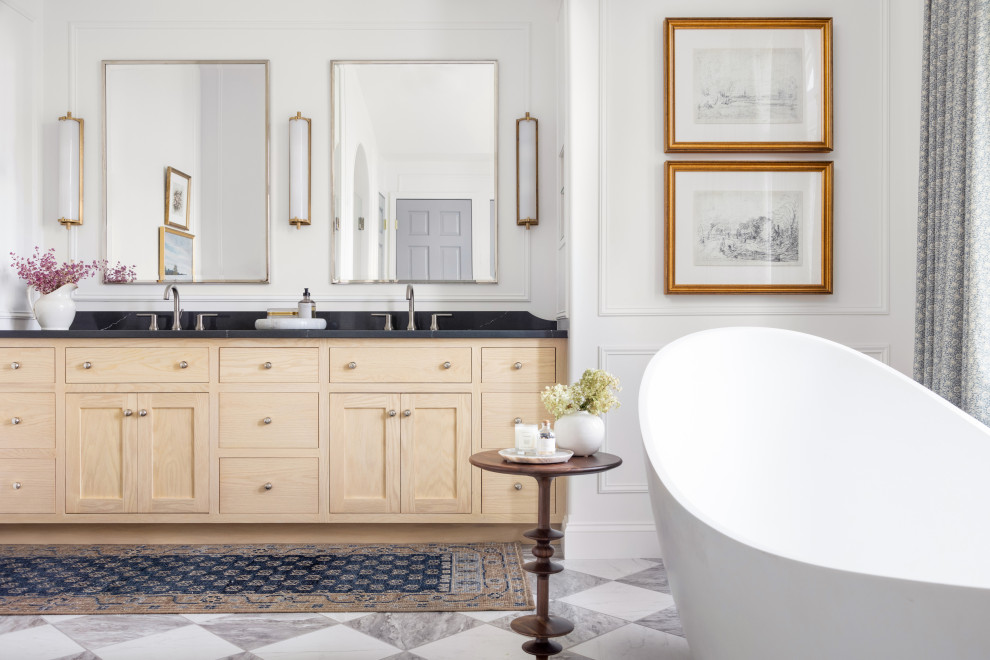 This is an example of a large transitional master bathroom in Other with shaker cabinets, light wood cabinets, a freestanding tub, an alcove shower, a one-piece toilet, white tile, ceramic tile, white walls, porcelain floors, an undermount sink, engineered quartz benchtops, white floor, a hinged shower door, black benchtops, a niche, a double vanity, a built-in vanity, vaulted and panelled walls.