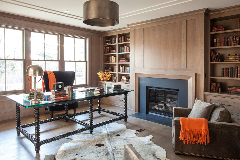 Photo of a transitional home office in New York with a library, medium hardwood floors, a standard fireplace and a freestanding desk.