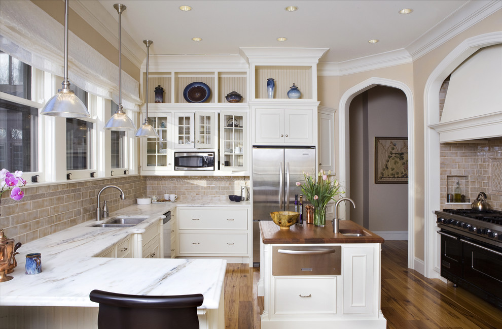 This is an example of a large traditional u-shaped separate kitchen in New York with glass-front cabinets, stainless steel appliances, marble benchtops, a double-bowl sink, white cabinets, beige splashback, subway tile splashback, medium hardwood floors, with island, brown floor and grey benchtop.