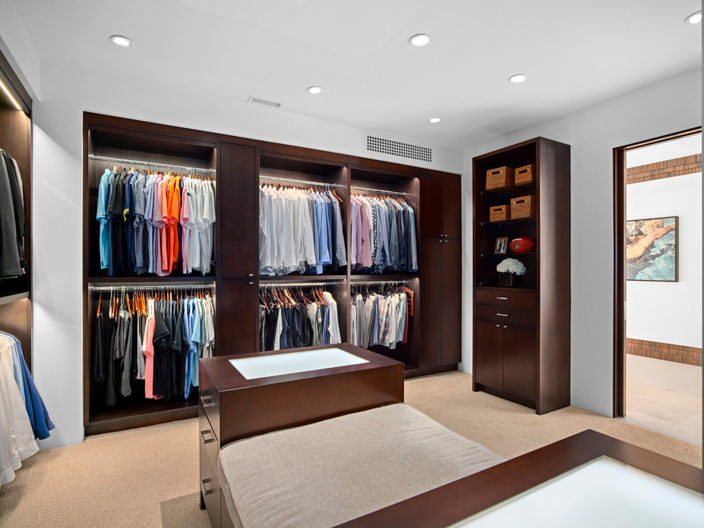 Tropical men's dressing room in Orange County with open cabinets, dark wood cabinets, carpet and beige floor.