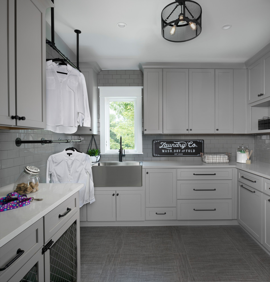 This is an example of a large transitional dedicated laundry room in Other with grey cabinets, solid surface benchtops, grey walls, grey floor, white benchtop, a farmhouse sink and shaker cabinets.