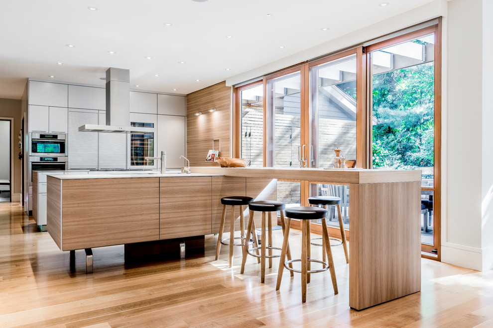 This is an example of a mid-sized contemporary single-wall open plan kitchen in Boston with flat-panel cabinets, grey cabinets, light hardwood floors, with island, beige floor, stainless steel appliances, wood benchtops and brown benchtop.