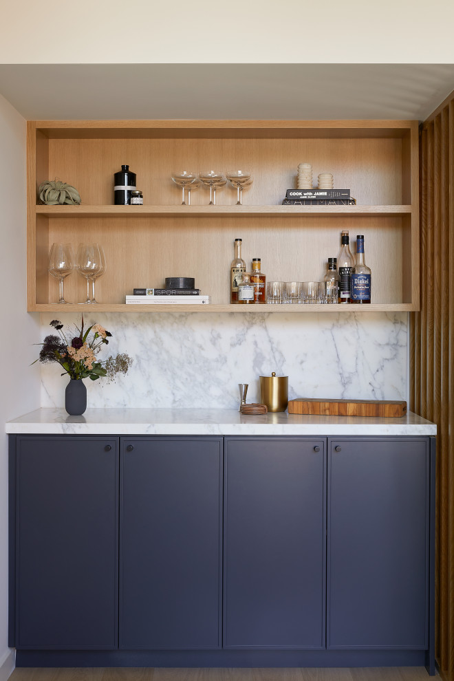 Design ideas for a small midcentury single-wall home bar in San Francisco with no sink, shaker cabinets, blue cabinets, marble benchtops, white splashback, marble splashback, light hardwood floors, brown floor and white benchtop.