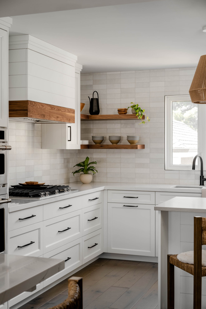 Design ideas for a mid-sized country l-shaped eat-in kitchen in Toronto with an undermount sink, shaker cabinets, white cabinets, quartz benchtops, white splashback, subway tile splashback, stainless steel appliances, dark hardwood floors, multiple islands, brown floor and grey benchtop.