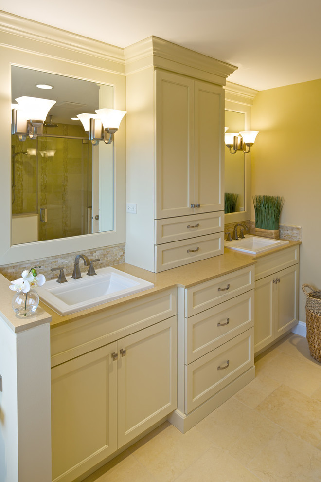 Mid-sized transitional master bathroom in New York with recessed-panel cabinets, white cabinets, solid surface benchtops, beige tile, a shower/bathtub combo, a one-piece toilet, a drop-in sink, beige walls and limestone floors.