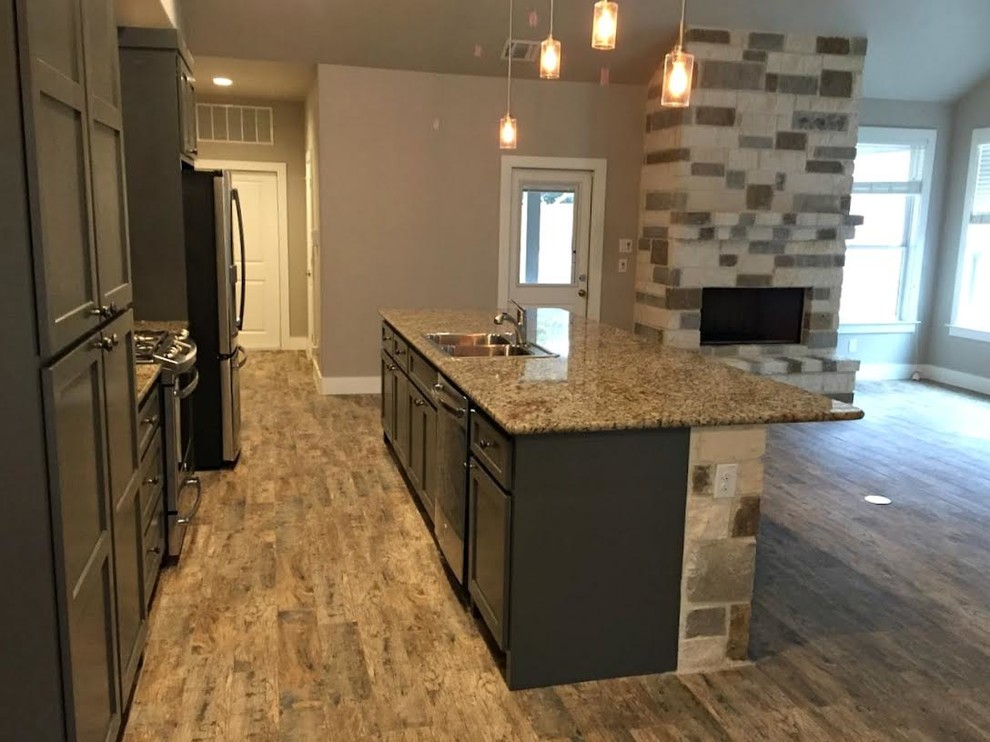 Example of a mid-sized transitional galley medium tone wood floor and brown floor open concept kitchen design in Austin with a double-bowl sink, shaker cabinets, gray cabinets, granite countertops, gray backsplash, glass tile backsplash, stainless steel appliances and an island