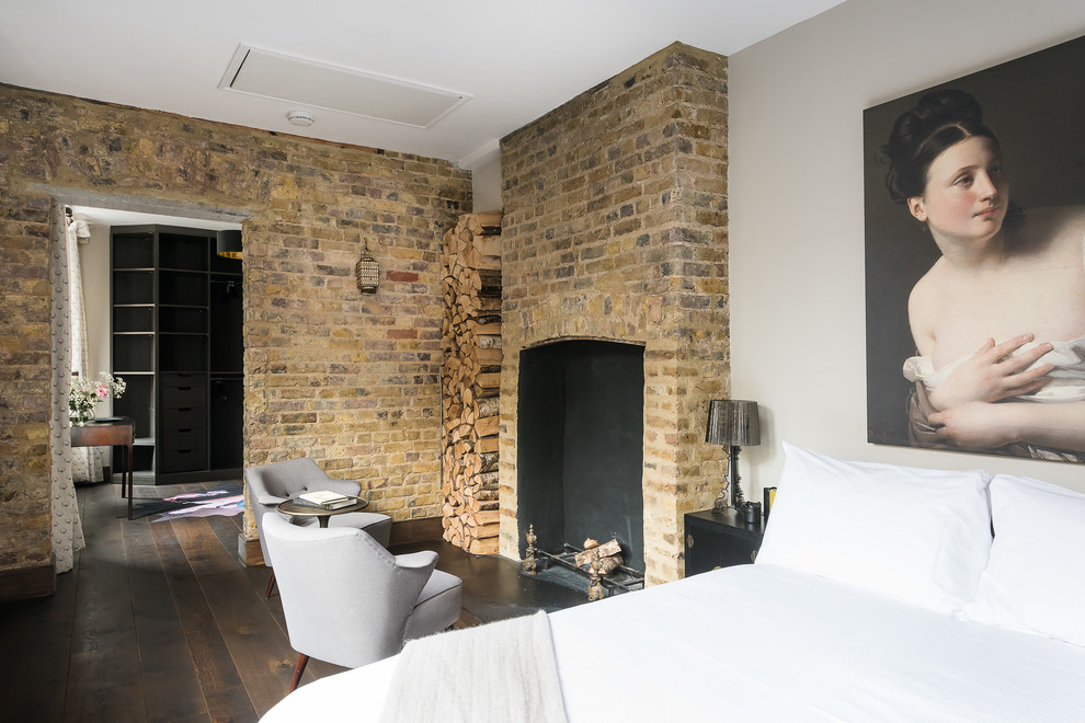 Photo of an eclectic master bedroom in London with dark hardwood floors, a standard fireplace and a brick fireplace surround.