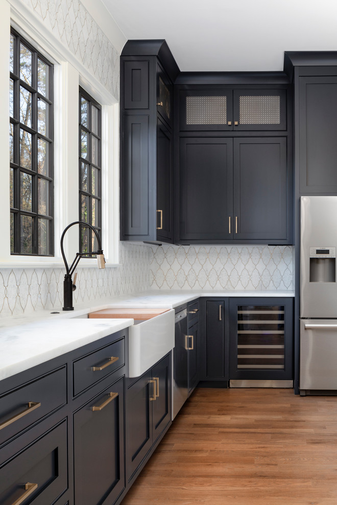 Design ideas for a mid-sized traditional l-shaped kitchen in Charlotte with a farmhouse sink, blue cabinets, marble benchtops, white splashback, mosaic tile splashback, stainless steel appliances, medium hardwood floors, brown floor and white benchtop.