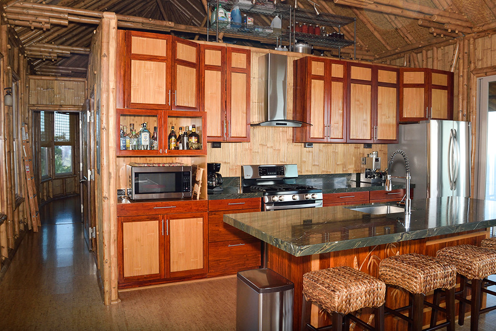 This is an example of a tropical galley open plan kitchen in Hawaii with an undermount sink, beaded inset cabinets, light wood cabinets, granite benchtops, grey splashback, stone slab splashback, stainless steel appliances, cork floors and with island.
