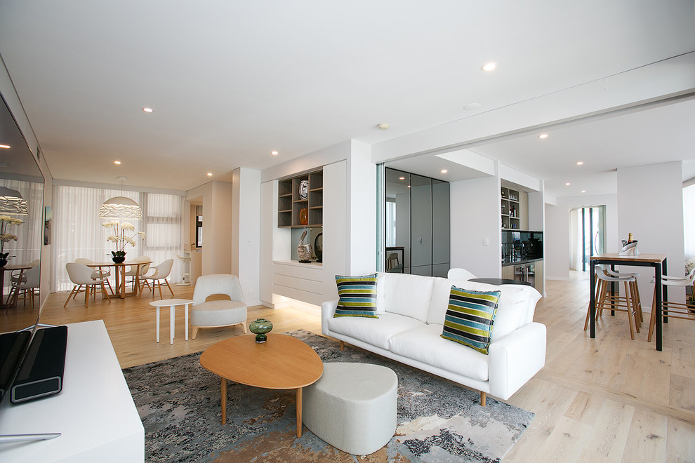 This is an example of a contemporary open concept living room in Newcastle - Maitland with white walls, light hardwood floors, a freestanding tv and beige floor.