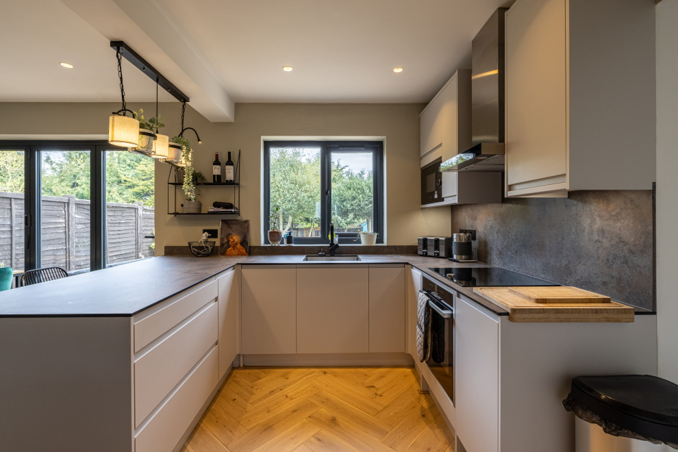 Esempio di una cucina abitabile contemporanea di medie dimensioni con lavello da incasso, elettrodomestici neri, parquet chiaro, penisola e pavimento beige