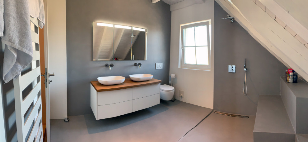 Duschbad With flächenbündigen Schrankfronten, weißen Schränken, bodengleicher Dusche, Wandtoilette, grauen Fliesen, Marmorfliesen, weißer Wandfarbe, Betonboden, Aufsatzwaschbecken, Waschtisch aus Holz, grauem Boden, offener Dusche, brauner Waschtischplatte, Duschbank, Doppelwaschbecken, schwebendem Waschtisch and Holzdecke in Nuremberg