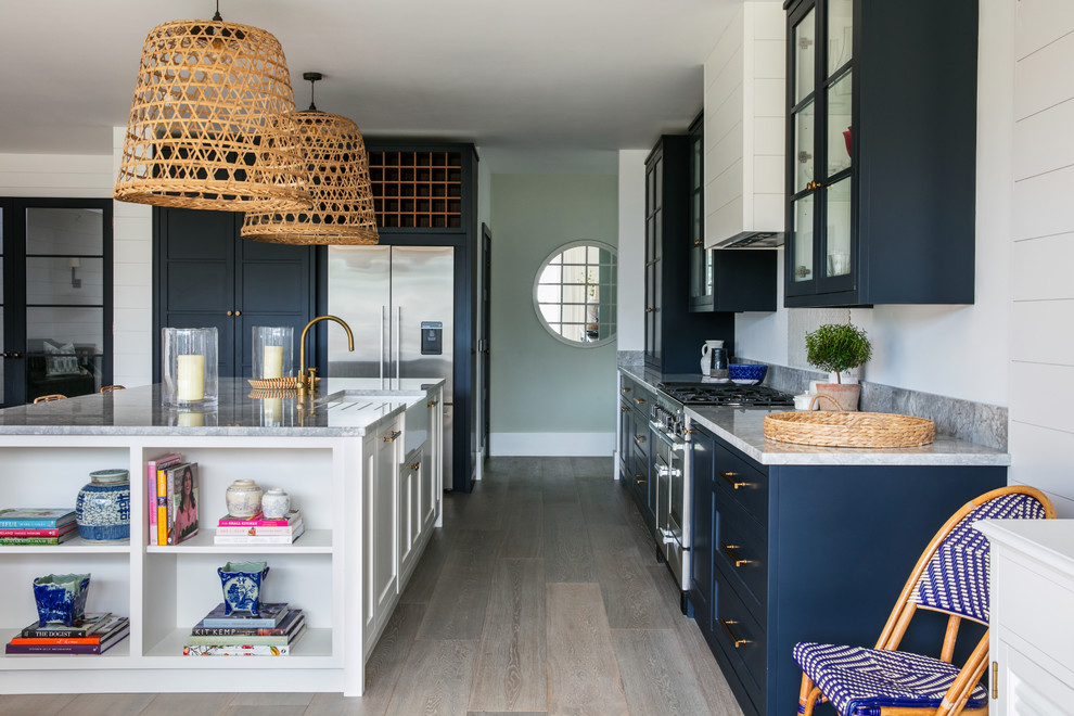 This is an example of a mid-sized beach style kitchen in Sussex with a farmhouse sink, blue cabinets, stainless steel appliances, light hardwood floors, with island, grey floor, grey benchtop and shaker cabinets.