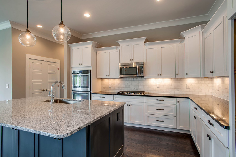 Inspiration for a mid-sized transitional dark wood floor kitchen remodel in Nashville with an undermount sink, shaker cabinets, white cabinets, granite countertops, white backsplash, stainless steel appliances and an island