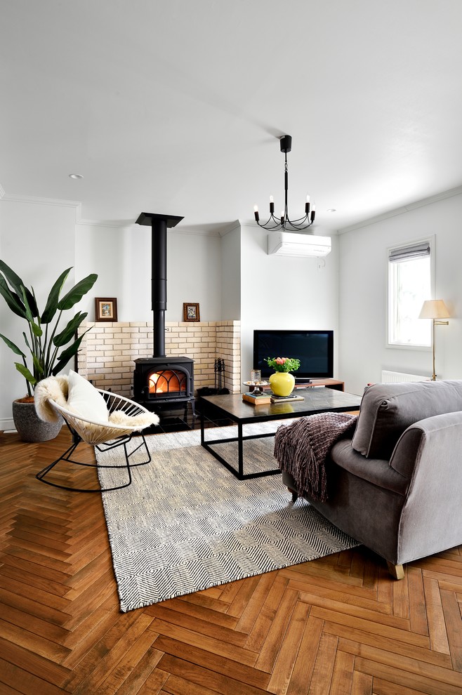 This is an example of a scandinavian formal open concept living room in Other with white walls, medium hardwood floors, a wood stove, a brick fireplace surround, a freestanding tv and brown floor.