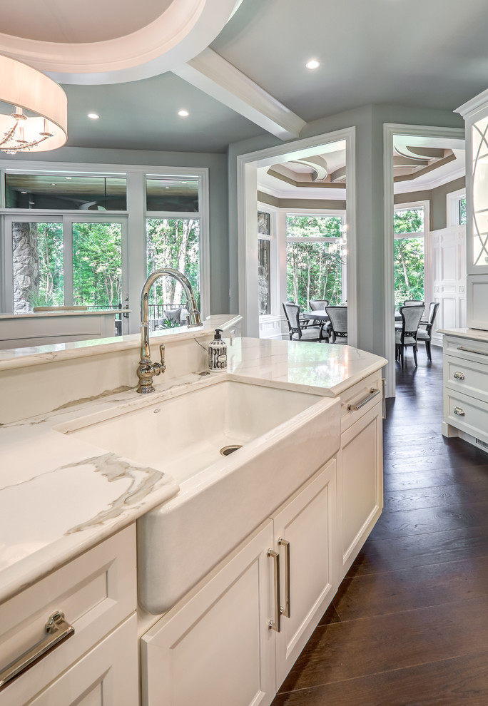 Photo of a large arts and crafts single-wall open plan kitchen in Columbus with a farmhouse sink, flat-panel cabinets, white cabinets, white splashback, panelled appliances, dark hardwood floors, multiple islands, brown floor and white benchtop.