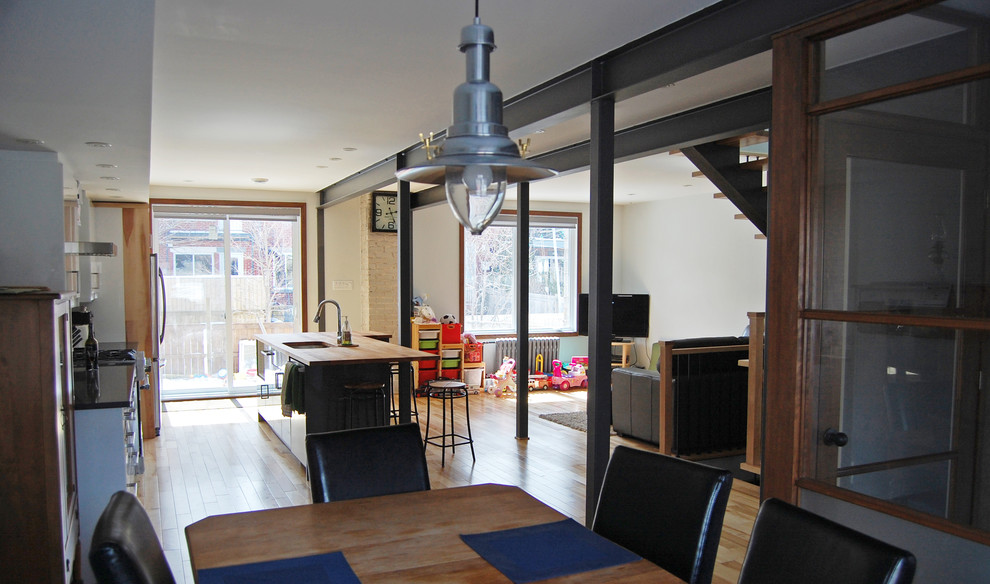 Photo of a mid-sized industrial dining room in Montreal with white walls, light hardwood floors and exposed beam.
