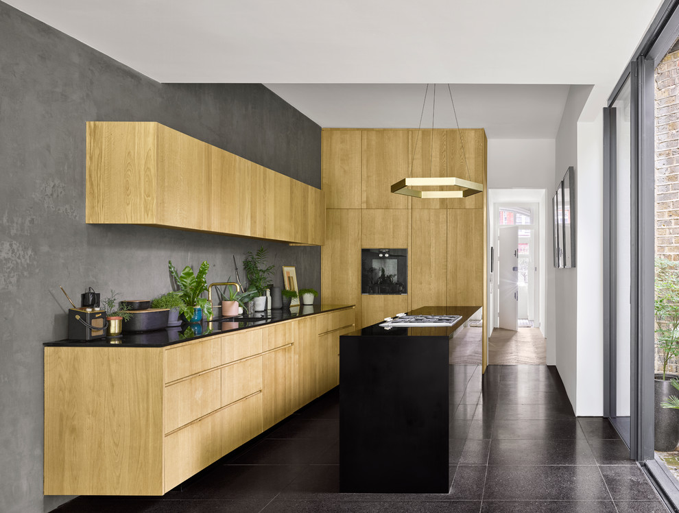 Inspiration for a contemporary l-shaped kitchen in London with an integrated sink, flat-panel cabinets, light wood cabinets, grey splashback, with island, black floor and black benchtop.