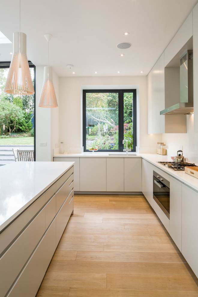 Mid-sized contemporary l-shaped kitchen in London with with island, flat-panel cabinets, quartz benchtops, stainless steel appliances, an undermount sink, light hardwood floors and white splashback.