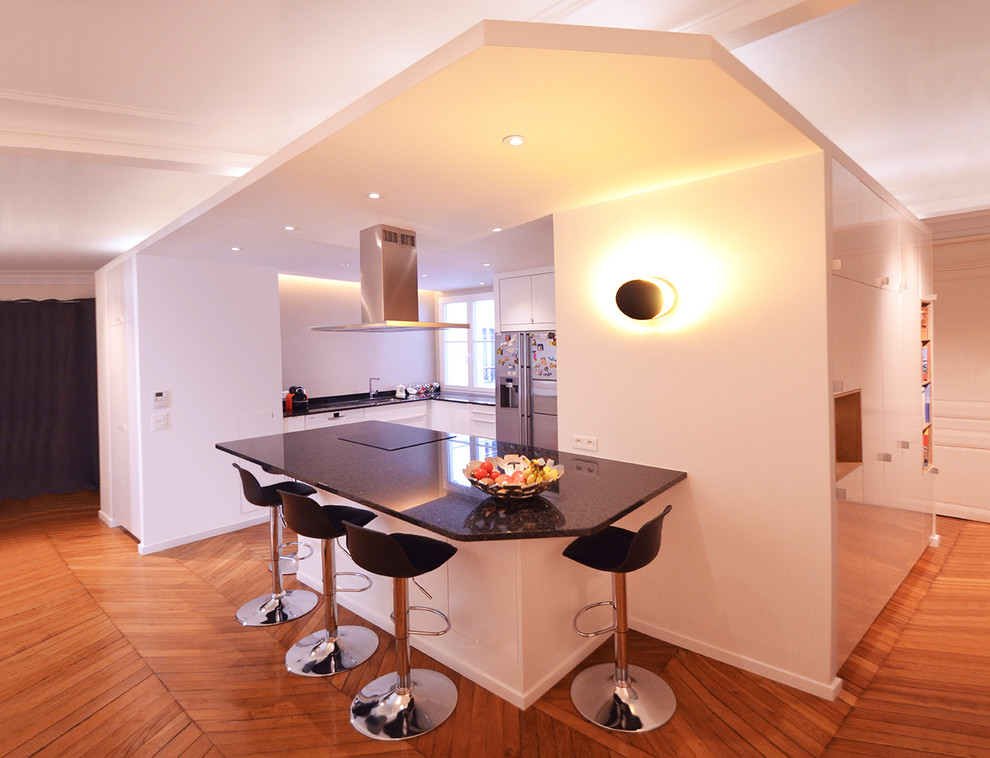 Cette photo montre cuisine américaine in U With un évier intégré, un placard à porte plane, des portes de placard blanches, un plan de travail en granite, une crédence beige, un électroménager en acier inoxydable, un sol en bois brun, îlot and un sol marron.