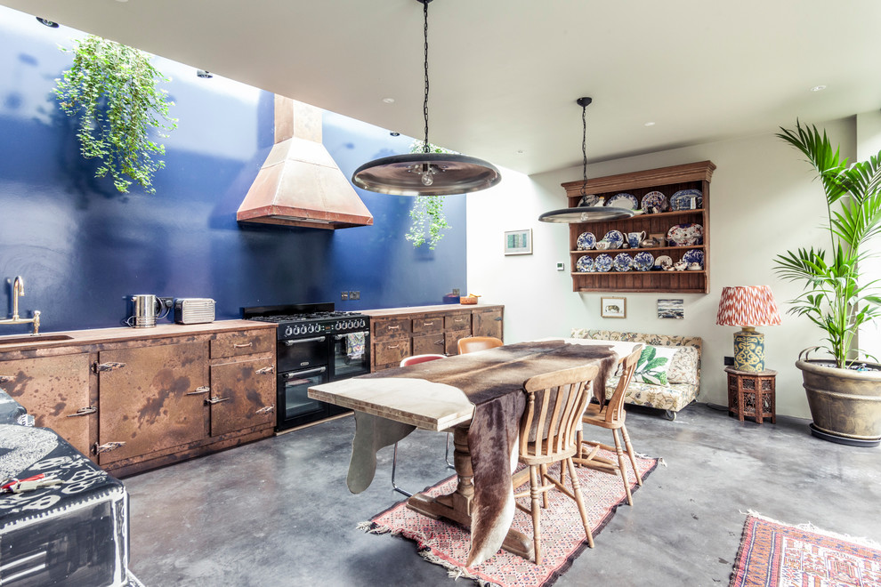 Design ideas for a mid-sized eclectic eat-in kitchen in London with distressed cabinets, blue splashback, black appliances, concrete floors, grey floor, flat-panel cabinets and no island.