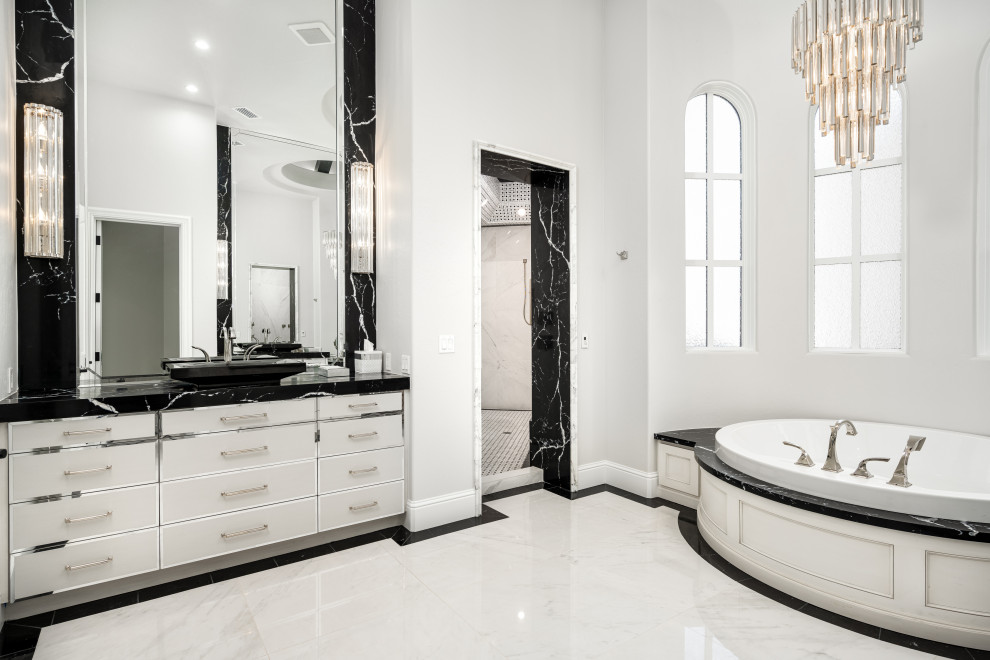 This is an example of an expansive modern master wet room bathroom in Phoenix with white cabinets, a drop-in tub, a one-piece toilet, black tile, marble, white walls, marble floors, a drop-in sink, marble benchtops, white floor, an open shower, black benchtops, a single vanity, a built-in vanity, coffered and panelled walls.