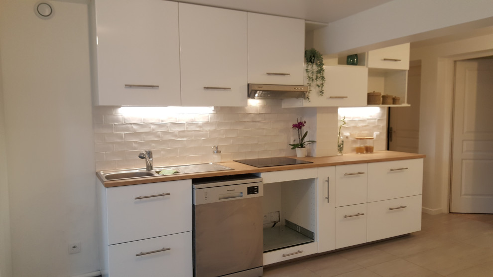 Mid-sized contemporary single-wall open plan kitchen in Paris with a single-bowl sink, flat-panel cabinets, white cabinets, laminate benchtops, white splashback, ceramic splashback, stainless steel appliances, ceramic floors and grey floor.